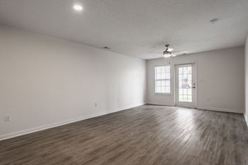 The living room of an empty house with white walls and a ceiling fan